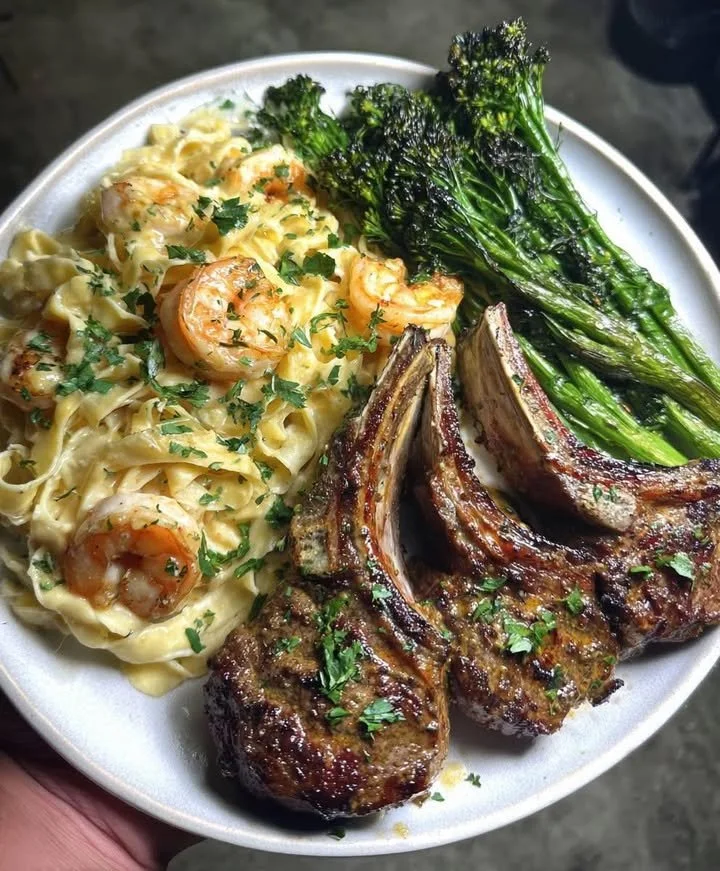 Garlic lamb chops served with shrimp Alfredo and roasted broccolini on a plate.