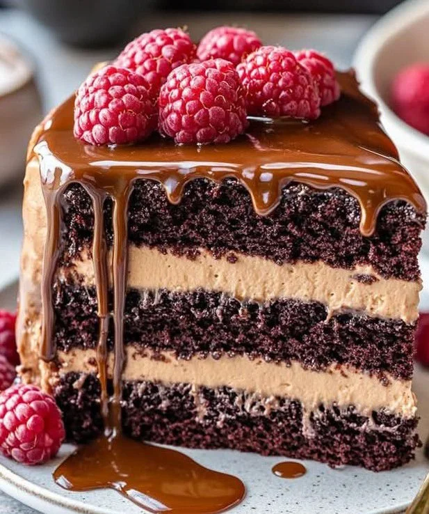 Chocolate Caramel Cream Raspberry Cake slice on a plate, garnished with raspberries