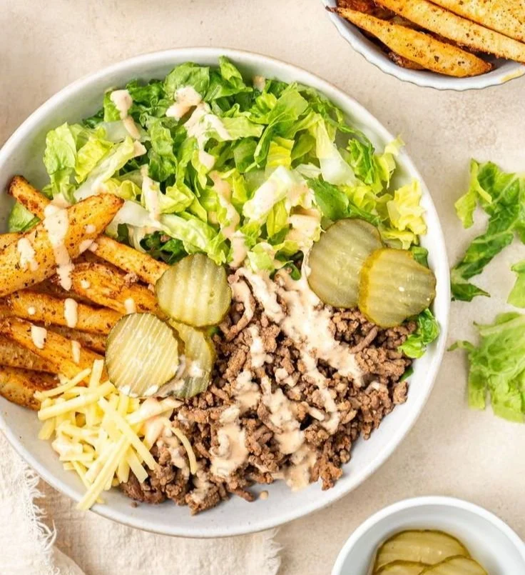 A colorful bowl featuring a juicy burger, fresh toppings, and vibrant veggies.